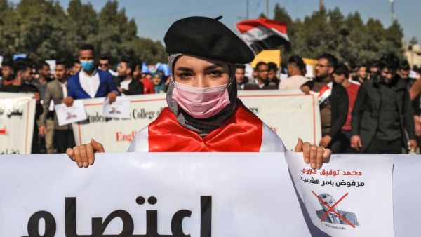 An Iraqi student wearing a beret and a surgical mask holds signs with a red X mark on the face of the new Iraqi prime minister designate Mohammad Allawi reading in Arabic "rejected by order of the people" during a demonstration against him in the central holy shrine city of Karbala on February 2, 2020. Mohammed SAWAF / AFP