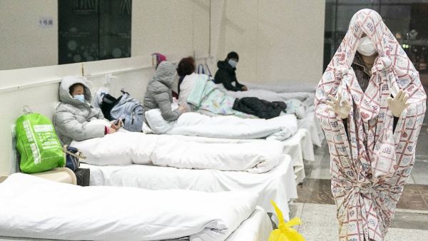 This photo taken on February 5, 2020 shows a patient (R) covered with a bed sheet at an exhibition centre converted into a hospital as it starts to accept patients displaying mild symptoms of the novel coronavirus in Wuhan in China's central Hubei province. China scrambled to find bed space for thousands of newly infected patients on February 6, as the toll from a deadly new virus jumped again with more than 28,000 people known infected nationwide and 563 deaths. STR / AFP