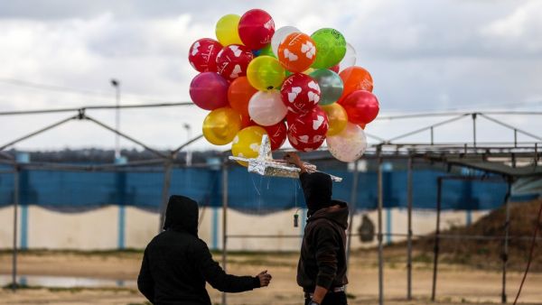 Masked Palestinians prepare to release an incendiary device near Gaza's Bureij refugee camp, along the Israel-Gaza border fence, on February 10, 2020. MAHMUD HAMS / AFP