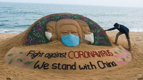 In this picture taken on February 10, 2020 Indian artist Sudarsan Pattnaik puts some final touches as he makes a sand sculpture depicting people wearing protective facemasks with a message reading 'Fight against coronavirus, We stand with China' at Puri beach in Puri. AFP