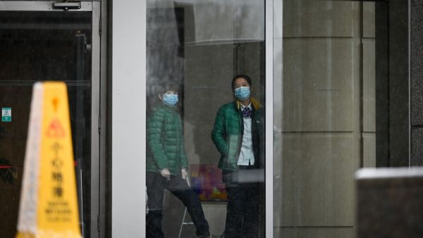 Two women wearing face mask look through a window in building in Beijing on February 14, 2020. The death toll from the COVID-19 coronavirus epidemic neared 1,400 on February 14, as the United States complained of a "lack of transparency" from Beijing over its handling of a crisis that has fuelled global panic. STR / AFP