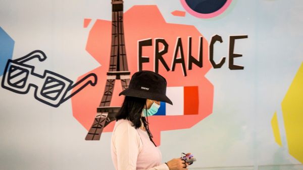 A woman, wearing a protective facemask amid fears over the spread of the COVID-19 coronavirus, walks in front of an advertisement board in Bangkok on February 17, 2020 featuring the Eiffel tower in France. Mladen ANTONOV / AFP