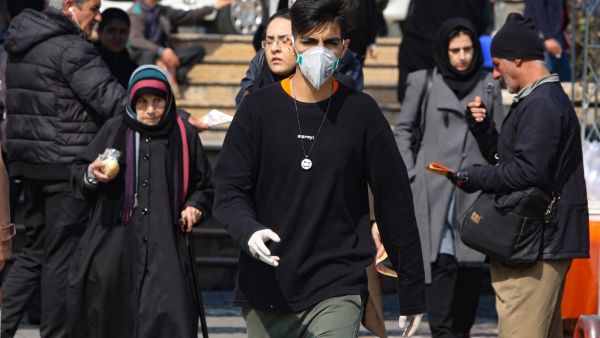 A young Iranian man wearing a protective mask and gloves, walks in a busy street in the capital Tehran on February 22, 2020. Iran today reported one more death among 10 new cases of coronavirus, bringing the total number of deaths in the Islamic republic to five and infections to 28. ATTA KENARE / AFP