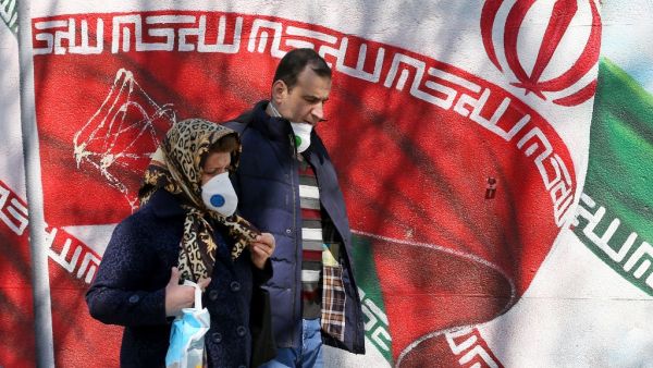 Iranians wearing masks walk past a mural displaying their national flag in Tehran on March 4, 2020. Iran has scrambled to halt the rapid spread of the COVID-19 virus, shutting schools and universities, suspending major cultural and sporting events, and cutting back on work hours.  ATTA KENARE / AFP