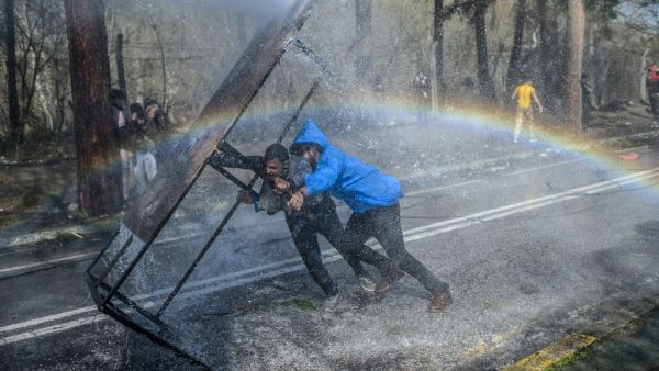 Migrants take cover behind a wooden board as Greek police uses water cannons to block them trying to break fences in the Turkey-Greece border province of Edirne on March 7, 2020. AFP/File