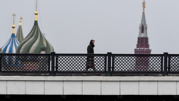 A man walks along a bridge over the Moskva river in front of St. Basil's Cathedral and the Kremlin in downtown Moscow on March 13, 2020. Yuri KADOBNOV / AFP