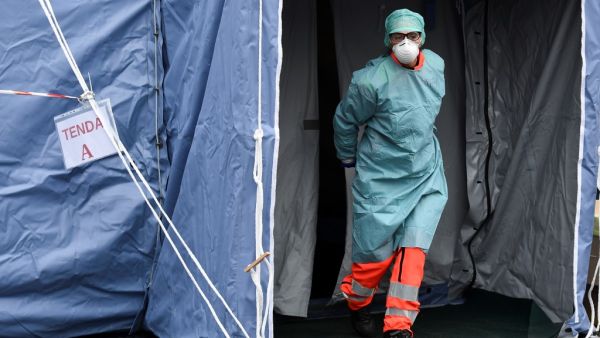 A hospital employees wearing a protection mask and gear exits a tent at a temporary emergency structure set up outside the accident and emergency department, where any new arrivals presenting suspect new coronavirus symptoms are being tested, at the Brescia hospital, Lombardy, on March 13, 2020. MIGUEL MEDINA / AFP