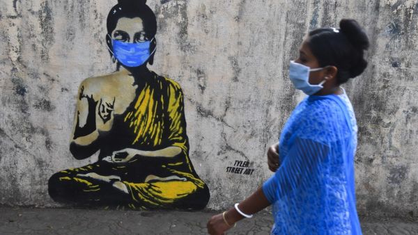 A resident wearing a facemask amid concerns over the spread of the COVID-19 novel coronavirus walks past a graffiti of Buddha wearing facemask, in Mumbai on March 16, 2020. INDRANIL MUKHERJEE / AFP