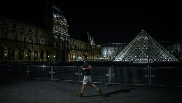 A man jogs past the Louvre Pyramid at night in Paris on March 18, 2020, as a strict lockdown came into in effect in France to stop the spread of COVID-19, caused by the novel coronavirus. A strict lockdown requiring most people in France to remain at home came into effect at midday on March 17, 2020, prohibiting all but essential outings in a bid to curb the coronavirus spread. The government has said tens of thousands of police will be patrolling streets and issuing fines of 135 euros ($150) for people wit