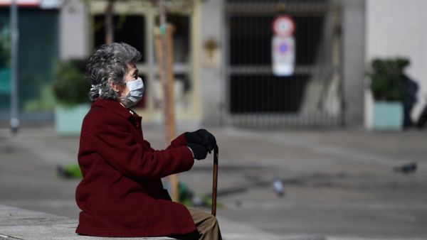 In this file photo taken on March 08, 2020 an elderly woman wearing a protective face mask sits on a bench in the city centre of Milan, after millions of people were placed under forced quarantine in northern Italy as the government approved drastic measures in an attempt to halt the spread of the COVID-19 outbreak, caused by the novel coronavirus that is sweeping the globe. While Italy is a country of senior citizens, the oldest in Europe according to statistics, and few of them live in retirement homes, t