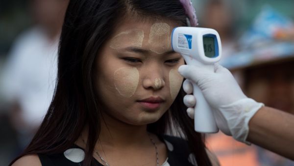 A woman wearing thanaka, a traditional facial cosmetic, has her temperature taken as a preventive measure against the COVID-19 novel coronavirus at a market in Yangon on March 21, 2020. Ye Aung Thu / afp