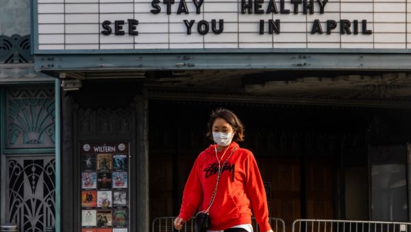 A woman walks wearing a mask to protect herself from the novel coronavirus (COVID-19) in front of a closed theater in Koreatown, Los Angeles, on March 21, 2020. All 40 million residents of California were on March 19 ordered to stay at home indefinitely in a bid to battle the coronavirus pandemic in the nation's most populous state. Apu GOMES / AFP