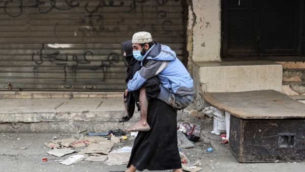 A woman carries a diabled man wearing a protective face mask in the market of the Palestinian refugee camp of Sabra, south of the capital Beirut, amid measures coordinated with Palestinian security forces to shut down all shops in a bid to limit the spread of the Covid-19 disease caused by the novel coronavirus, on march 22, 2020. ANWAR AMRO / AFP