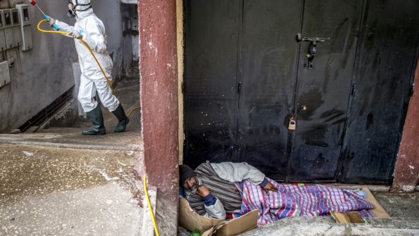 A homeless man sleeps on the side of a road as a Moroccan health ministry worker disinfects the wall of a building in the capital Rabat on March 22, 2020. A public health state of emergency went into effect in the Muslim-majority country late on March 20, and security forces and the army have been deployed on the streets to combat the spread of COVID-19 coronavirus disease. People have been ordered to stay at home, and restrictions on public transport and travel between cities are also in place. FADEL SENNA