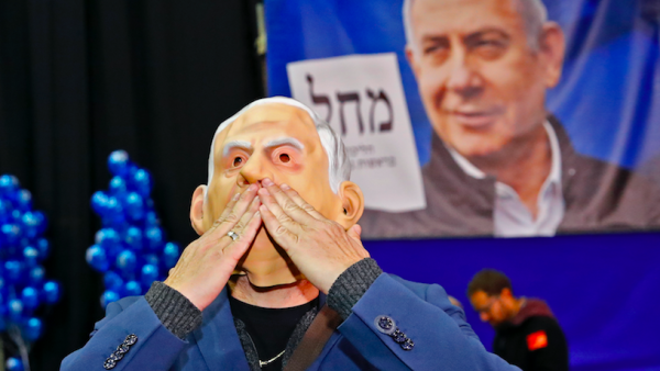 A man wearing a "Benjamin Netanyahu" face mask blows kisses as he stands before a giant Likud party election poster showing the face of its leader Prime Minister Netanyahu at the Likud's electoral headquarters in the coastal city of Tel Aviv on March 2, 2020, after polls officially closed. Exit polls by three Israeli television networks, released after polls closed, gave Likud between 36 and 37 seats in Israel's 120-member parliament against Blue and White's estimated 32 or 33. Jack GUEZ / AFP