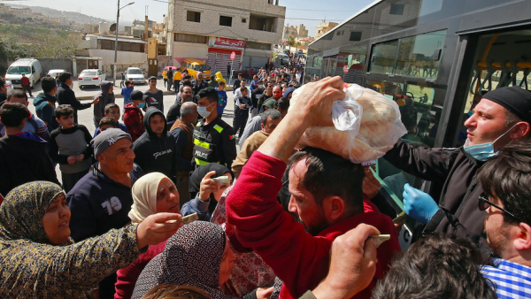 People queue to buy subsidised bread from a municipal bus in the Marka suburb in the east of Jordan's capital Amman on March 24, 2020, as the kingdom announced it would deliver bread and water supplies after the government decided to indefinitely extend a curfew amidst efforts to contain COVID-19 coronavirus disease. Khalil MAZRAAWI / AFP