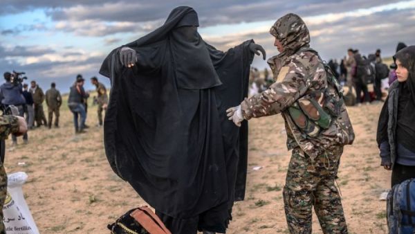 مقاتلة من "قسد" تفتش امرأة من عوائل داعش بأحد معسكرات الاحتجاز في سوريا