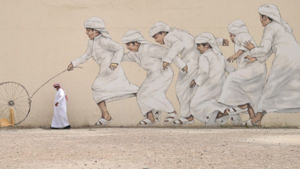 An Emirati man, wearing a protective face-mask, walks past a graffiti in Dubai on March 28, 2020. KARIM SAHIB / AFP