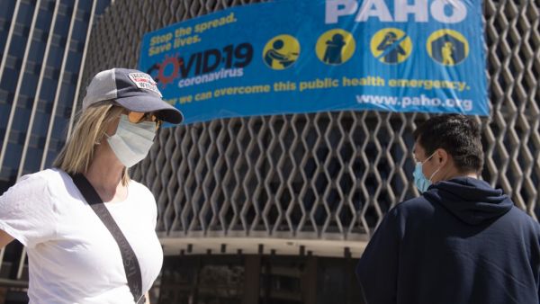 People wearing masks walk past a coronavirus awareness sign outside the World Health Organization in Washington, DC on March 30, 2020. The novel coronavirus, which has infected at least 155,252 people in the US, is thought to have been transmitted to humans by pigs, civets, or pangolins at the Huanan Seafood Wholesale Market in Wuhan, China. ANDREW CABALLERO-REYNOLDS / AFP