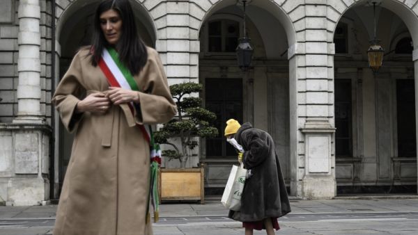 Turin mayor Chiara Appendino (L) stands at attention as an elderly woman walks past during a minute of silence at noon on March 31, 2020 in Turin as flags are being flown at half-mast in cities across Italy to commemorate the victims of the virus, during the country's lockdown aimed at curbing the spread of the COVID-19 infection, caused by the novel coronavirus. Marco BERTORELLO / AFP