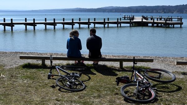 People sit in front of an empty swimming and sun pier near the shore of lake Starnberger See in Percha, southern Germany during warm weather with temperatures reaching 20 degrees celsius on April 5, 2020. AFP