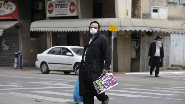 An ultra-Orthodox Jewish man wearing a protective mask, walks by carrying bags of shopping in the religious Israeli city of Bnei Brak, near Tel Aviv, on April 06, 2020 during the novel coronavirus pandemic crisis. More than 7,000 cases of COVID-19, including 40 deaths, have been officially declared in Israel, half of which according to local media, are ultra-Orthodox Jews, prompting the Prime Minister on April 3, to give a green light for amry deployment in the city, considered the centre of the country's n
