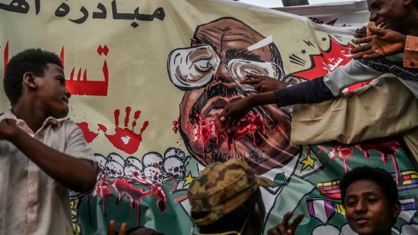 In this file photo taken on April 19, 2019, Sudanese protesters gesture in front of a banner depicting ousted and detained president Omar al-Bashir, during a protest outside the army headquarters in the capital Khartoum. AFP/File