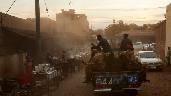 SSNPS (South Sudan National Police Service) police drive on pickup trucks past street vendors while patrolling the streets of Juba, South Sudan on April 9, 2020. South Sudanese police are enforcing a night curfew which was recently introduced by the government in order to slow the spread of the COVID-19 coronavirus. Alex McBride / AFP