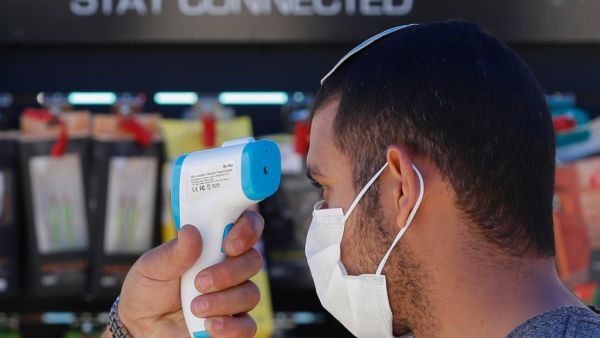 A worker checks the body temperature of a costumer before allowing him to enter the Electro Slil hardware store in Jerusalem during the COVID-19 pandemic, on April 20, 2020. Israel today allowed a reopening of high street shops, schools for children with special educational needs and a resumption of small-scale prayer meetings. EMMANUEL DUNAND / AFP
