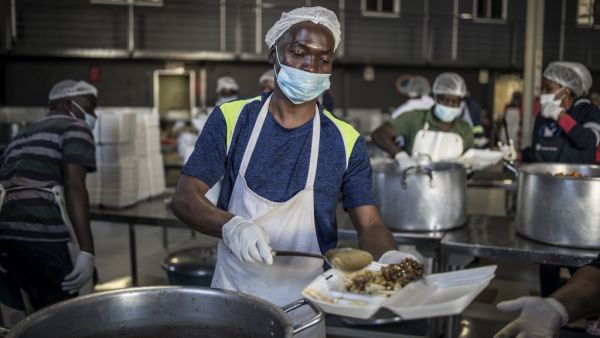 A volunteer pours a ladle of food into a container as he prepares packed relief meals at the Meals on Wheels Community Services South Africa in Johannesburg, on April 21, 2020. AFP