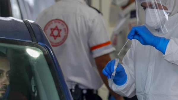 A paramedic with Israel's Magen David Adom medical service tests a man for COVID-19 at a drive-through site in Jabal Mukaber [Ahmad Gharabli/AFP]
