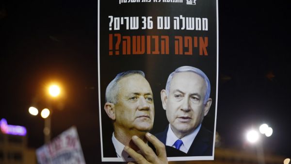 A protester carries a placard with a picture of Prime Minister Benjamin Netanyahu (R) and his rival-turned-partner Benny Gantz, during a demonstration in Tel Aviv's Rabin Square on May 2, 2020, in favour of the Supreme Court to consider tomorrow to block the coalition government agreed between the two men. If the expanded panel of 11 judges set to hear the case deems the coalition deal invalid, Israel may be forced to hold its fourth election in less than two years. JACK GUEZ / AFP