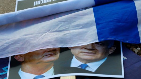 A rolled Israeli flag lies upon a placard left on the street with a picture of Prime Minister Benjamin Netanyahu and his rival-turned-partner Benny Gantz, during a demonstration in Tel Aviv's Rabin Square on May 2, 2020, in favour of the Supreme Court to consider tomorrow to block the coalition government agreed between the two men. If the expanded panel of 11 judges set to hear the case deems the coalition deal invalid, Israel may be forced to hold its fourth election in less than two years. JACK GUEZ / AF