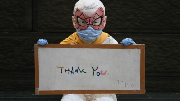 A statue of a child wearing a face mask and a spider man mask holds a "thank you" note for medical and essential workers outside The Mount Sinai Hospital during the the COVID-19 shutdown on May 4, 2020 in New York City. Angela Weiss / AFP