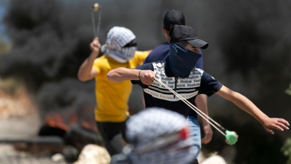 Tires burn as Palestinian youths use sling shots to hurl rocks at Israeli troops, during clashes with them in the West-Bank village of Kfar Qaddum, following a weekly demonstration against the expropriation of Palestinian land by Israel, on May 8, 2020. JAAFAR ASHTIYEH / AFP