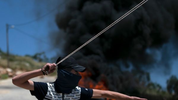 Tires burn as a Palestinian youth uses a sling shot to hurl rocks at Israeli troops, during clashes with them in the West-Bank village of Kfar Qaddum, following a weekly demonstration against the expropriation of Palestinian land by Israel, on May 8, 2020. JAAFAR ASHTIYEH / AFP
