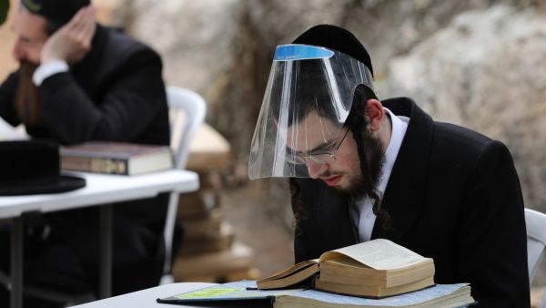 Ultra-Orthodox Jews wearing protective gear and observing social distancing amid the COVID-19 pandemic, study the Talmud and rabbinic literature at an improvised outdoors Kollel (gathering place for religious studies) at a park in their Ultra-orthodox neighbourhood in Jerusalem, on May 11, 2020. MENAHEM KAHANA / AFP