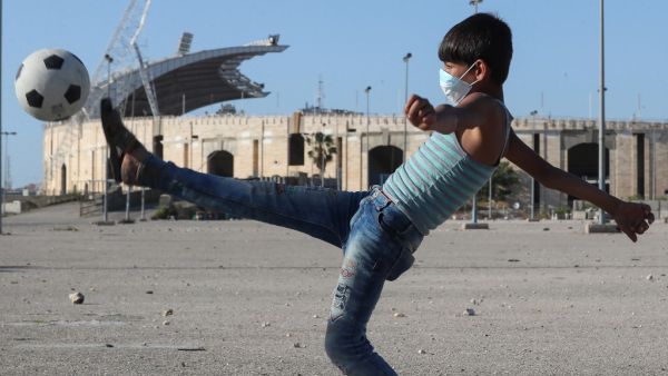 A mask-clad boy kicks a ball in front of the Camille Chamoun Sports City Stadium in the Lebanese capital Beirut amid the ongoing COVID-19 pandemic, on May 11, 2020. Lebanon ordered a four-day-long lockdown to stem the spread of the coronavirus after recording an uptick in infections in recent days amid eased restrictions. AFP