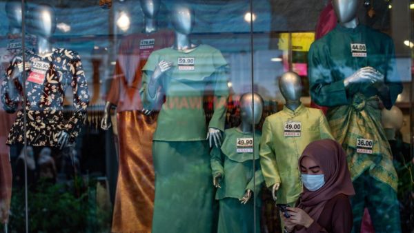 A woman wears a face mask as a preventive measure against the spread of the COVID-19 coronavirus as she browses her phone in front of a shop selling Malaysian cultural outfits called Baju Melayu and Baju Kurung ahead of the Islamic Eid al-Fitr festival, which marks the end of the holy month of Ramadan, in Kuala Lumpur on May 13, 2020. Mohd RASFAN / AFP