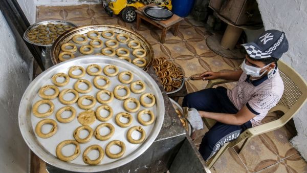 A Palestinian man, wearing protective face masks and gloves during the COVID-19 pandemic, bakes traditional cookies in preparation for the upcoming Eid al-Fitr holiday which marks the end of the Islamic holy month of Ramadan, in the southern Gaza Strip city of Rafah on May 17, 2020. SAID KHATIB / AFP