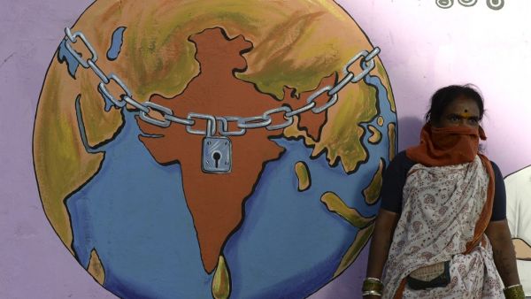 A labourer with her face covered waits for a local transport beside a graffiti depicting a world under lockdown, during a nationwide lockdown as a preventive measure against the COVID-19 coronavirus, on the outskirts of Hyderabad on May 29, 2020. NOAH SEELAM / AFP