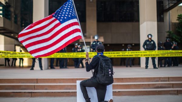 A demonstrator holding a US flag kneels in front of the Police at the Anaheim City Hall on June 1, 2020 in Anaheim, California, during a peaceful protest over the death of George Floyd. (Apu GOMES / AFP)
