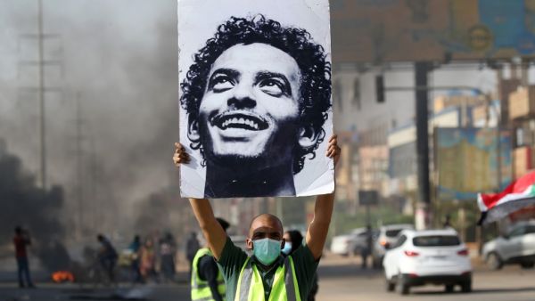 A mask-clad man holds a picture of a Abdulsalam Kisha, a Sudanese protester who was killed in a raid on an anti-government sit-in in 2019, during a protest in the Riyadh district in the east of the capital Khartoum on the anniversary of the raid on June 3, 2020. One year after the 25-year-old Abdulsalam's killing in the dispersal of Sudan's main protest camp, his father Kisha is still holding out hope that the killers be brought to justice as he calls for an international probe. The young protester was kill