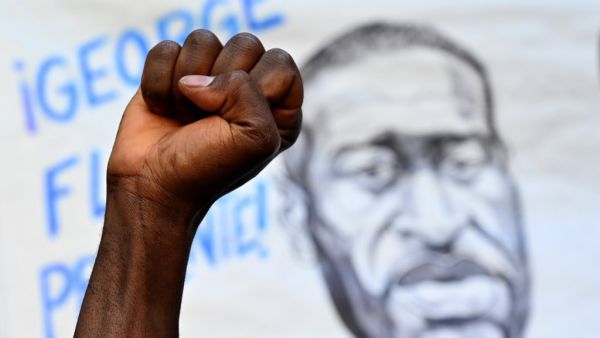 A man raises his fist in front of a portrait of George Floyd, an unarmed black man who died after a white policeman knelt on his neck during an arrest in the US, in Madrid, on June 7, 2020 during a demonstration against racism and in solidarity with the Black Lives Matter movement. Gabriel BOUYS / AFP
