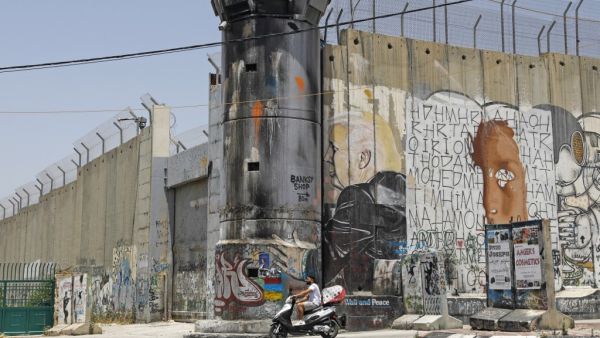 A Palestinian man rides his motorcycle past a mural painting of US President Donald Trump on Israel's controversial separation barrier in the West Bank city of Bethlehem on June 8, 2020. AHMAD GHARABLI / AFP