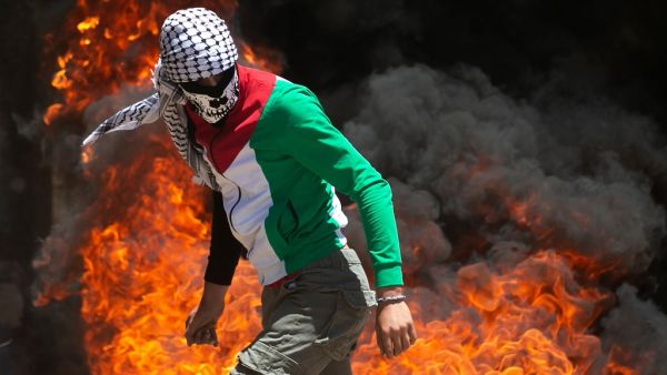 A Palestinian protester walks near burning tires during clashes with Israeli forces during a demonstration in the village of Kfar Qaddum in the Israeli-occupied West Bank, against the Jewish state's plans to annex part of the territory, on June 12, 2020. Israel intends to annex West Bank settlements and the Jordan Valley, as proposed by US President Donald Trump, with initial steps slated to begin from July 1. JAAFAR ASHTIYEH / AFP