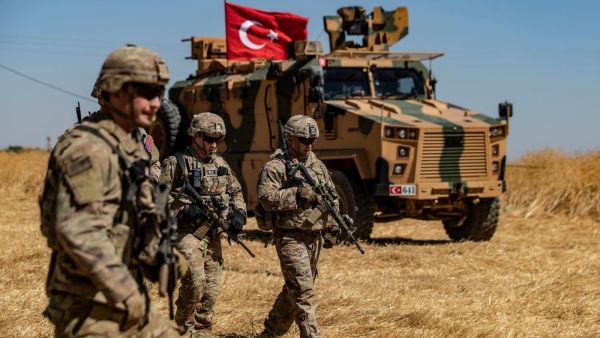 US troops walk past a Turkish military vehicle on the outskirts of Tal Abyad town along the Syrian-Turkish border on 8 September (AFP)