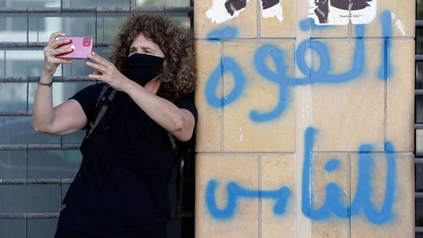 Lebanese director Carol Mansour uses her phone to film while wearing a face mask and standing by graffiti reading in Arabic “power to the people”, in the centre of the capital Beirut. (AFP)
