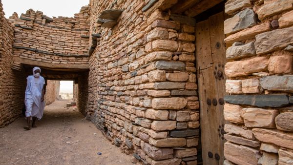 White dressed Beduin in front of historic bricked houses at world hertiage site Tichitt, Mauritania  (Shutterstock)