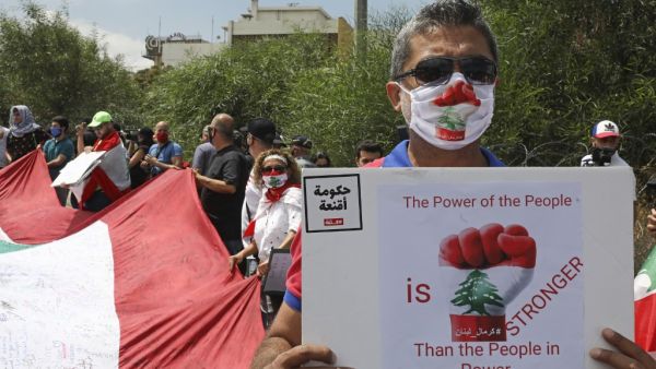 Lebanese anti-government protesters carry a large national flag and placards during a demonstration near the presidential palace in Baabda, east of Beirut, on June 25, 2020. ANWAR AMRO / AFP